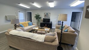 A living room with beige sofas, a coffee table, a TV, and a lamp. - Cozy Cottage, Quiet and Peaceful, Minutes from Lake Guntersville (Grant)