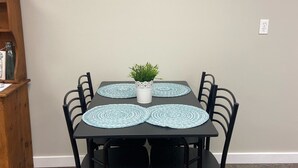 A dining area with a table set for four, surrounded by black chairs. Above the table, there are two wall-mounted decorative items with flowers and a framed picture of a sunset. - Cozy Cottage, Quiet and Peaceful, Minutes from Lake Guntersville (Grant)