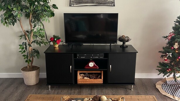 A living room with a flat-screen TV on a black entertainment unit, a potted plant, a small Christmas tree, and a coffee table with a book and a magazine. - Cozy Cottage, Quiet and Peaceful, Minutes from Lake Guntersville (Grant)