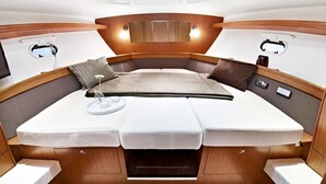 A compact, well-lit interior with a central bed, wooden paneling, and a small table with a lamp. - Yacht "BAVARIA 37 SPORT "RIBELLE"" in Sardinia - with a sporty design (Olbia)