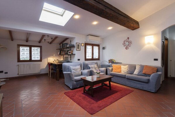 Un salón con techo alto, vigas a la vista, tragaluces, chimenea, sofá, mesa de centro y radiador.