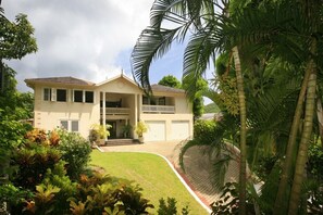 A two-story house with a balcony, surrounded by lush greenery and a well-maintained lawn.