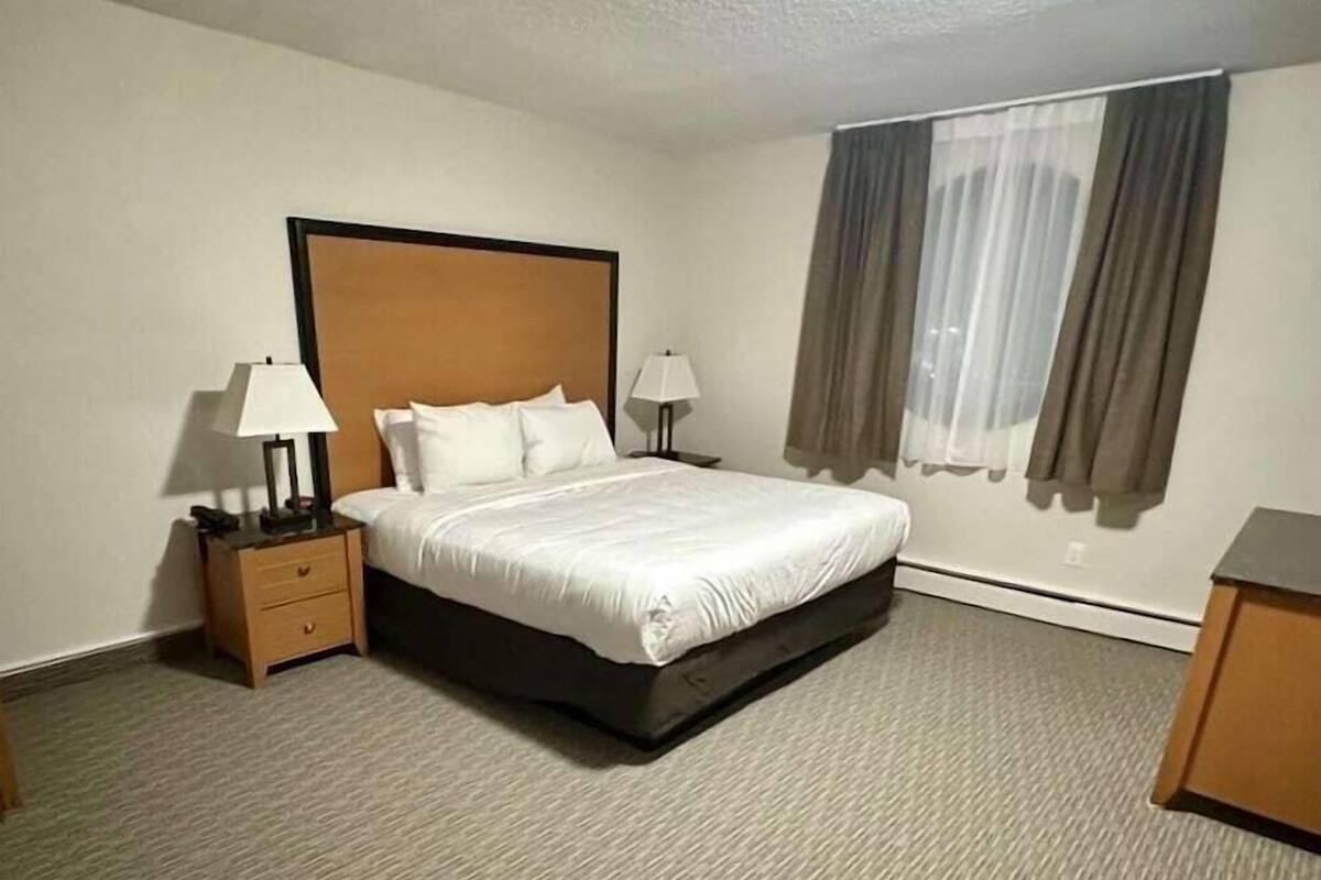 A hotel room with a bed, two bedside tables with lamps, a window with curtains, and a carpeted floor.