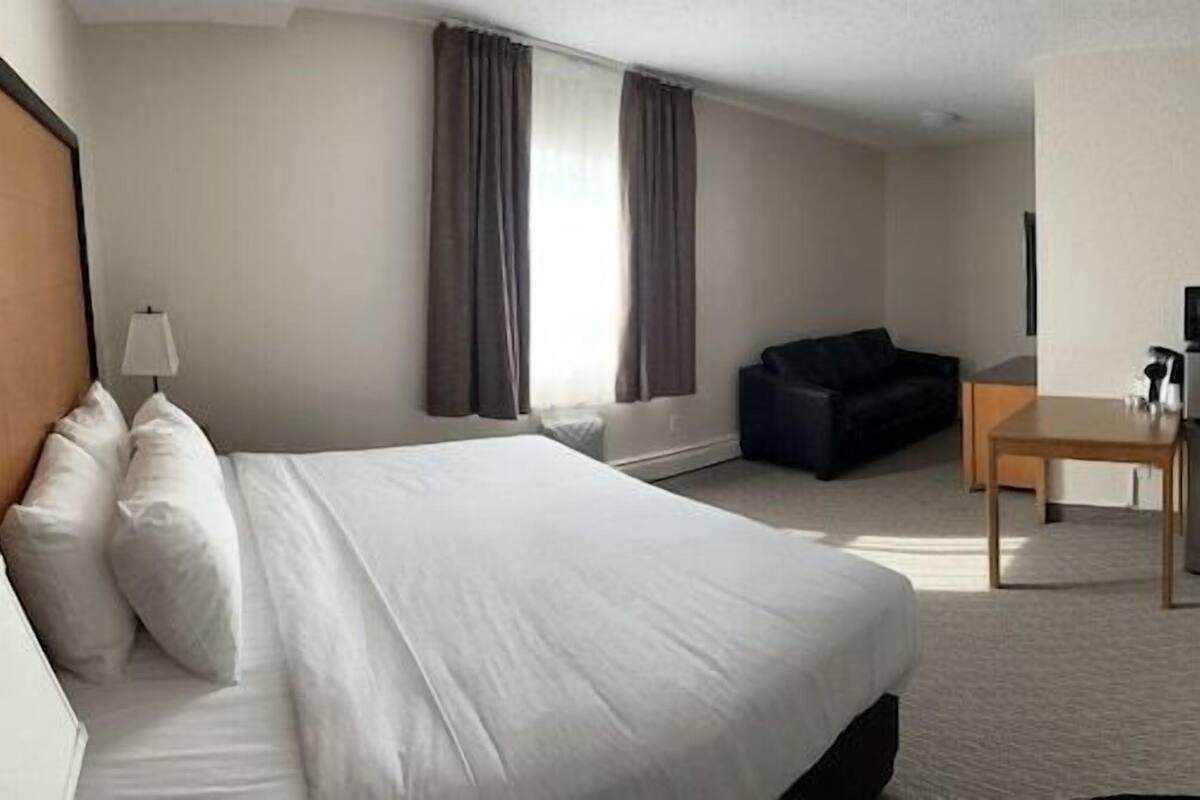 A hotel room with a bed, a desk, a chair, a microwave, a small table, and a bathroom with a toilet and sink.