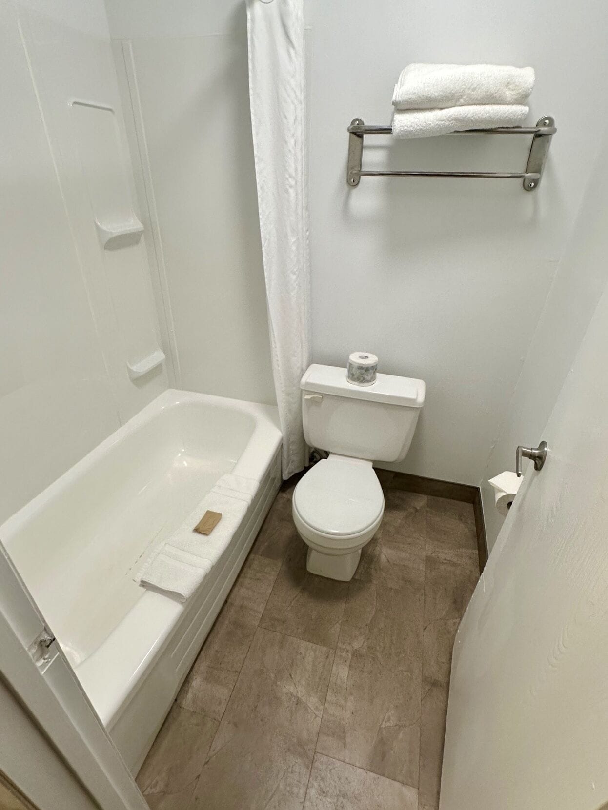 Un baño pequeño y limpio con bañera blanca, inodoro y zona de ducha.