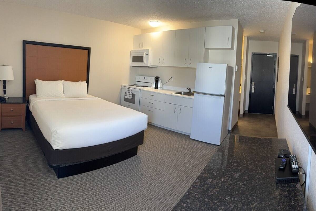 A hotel room with a bed, a kitchenette, and a bathroom.