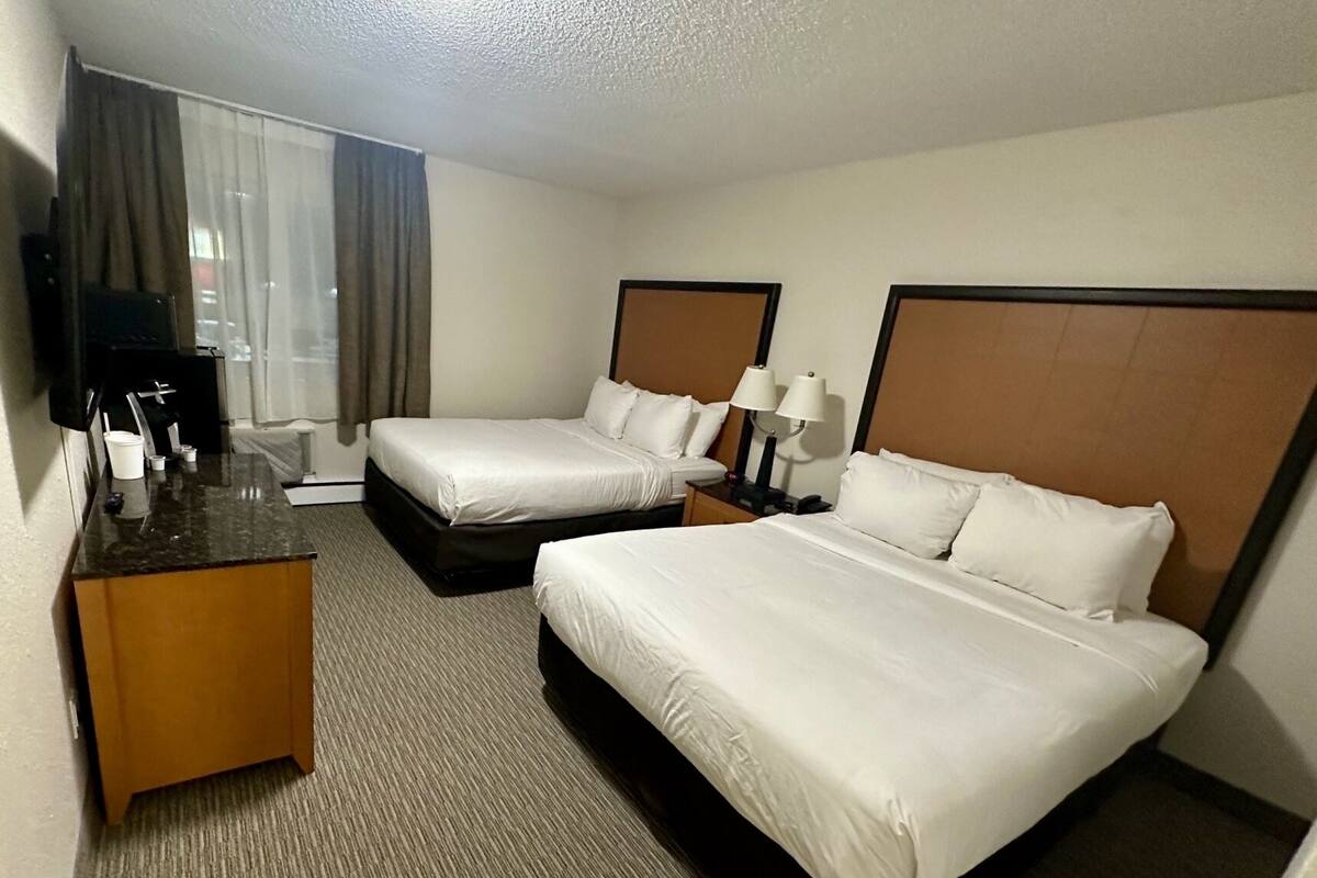 A hotel room with two beds, a desk with a chair, a television, and a window with curtains.