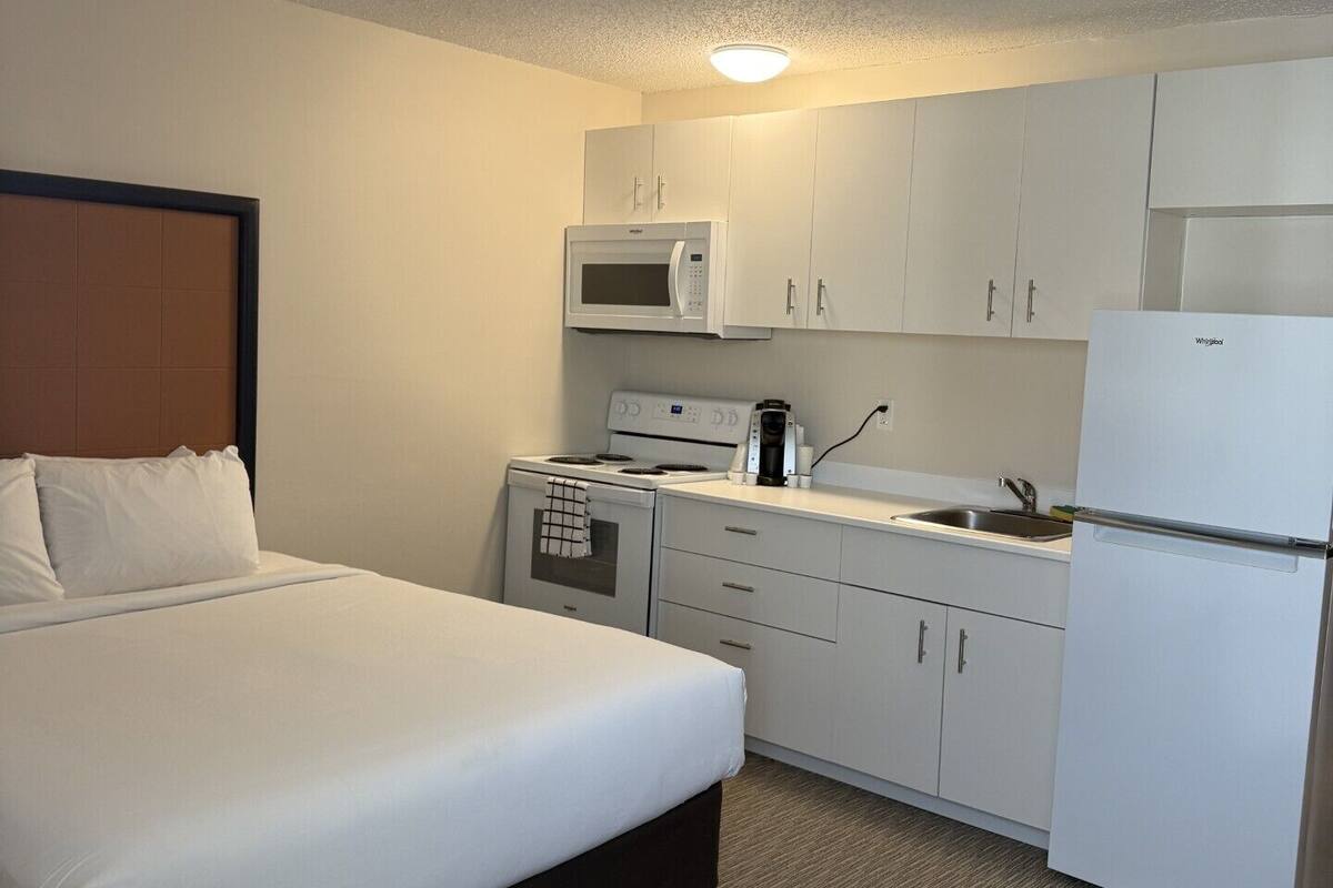 A compact hotel room with a bed, kitchenette, and a microwave.