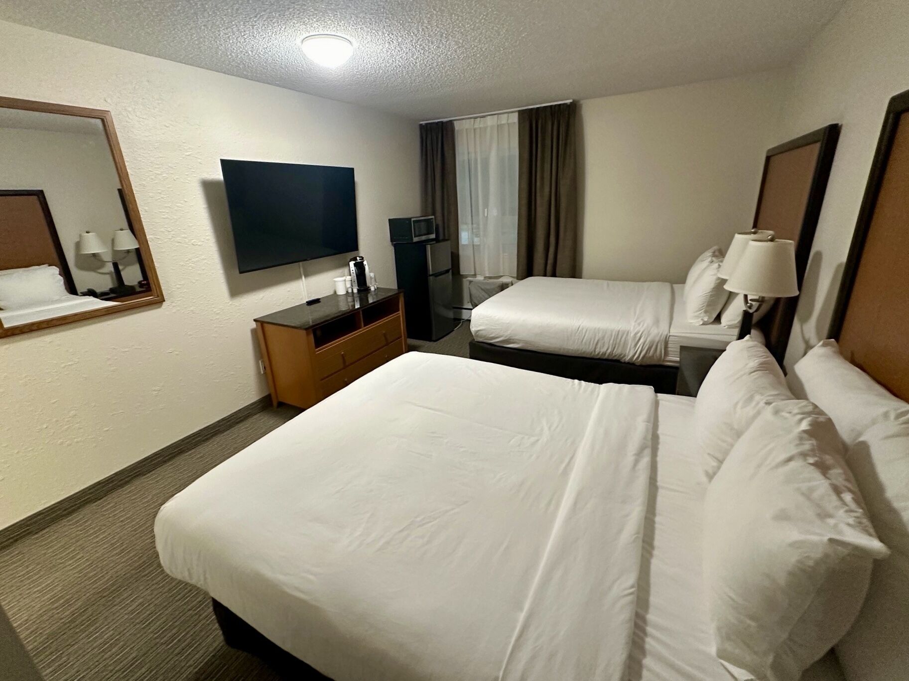 A hotel room with two beds, a TV, a desk with a coffee maker, and a mirror.