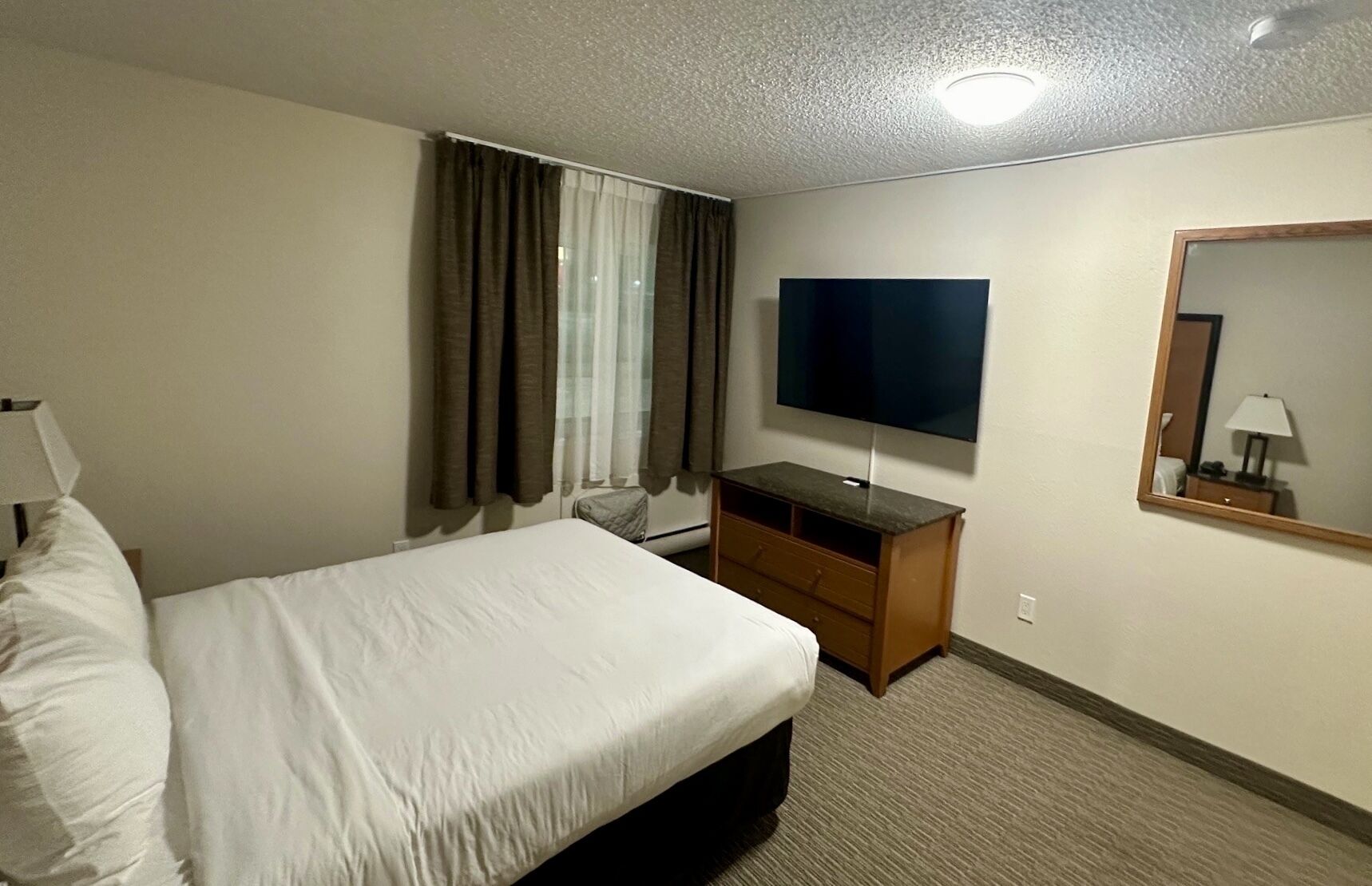 A hotel room with a large bed, a flat-screen TV, a wooden dresser, and a mirror on the wall.
