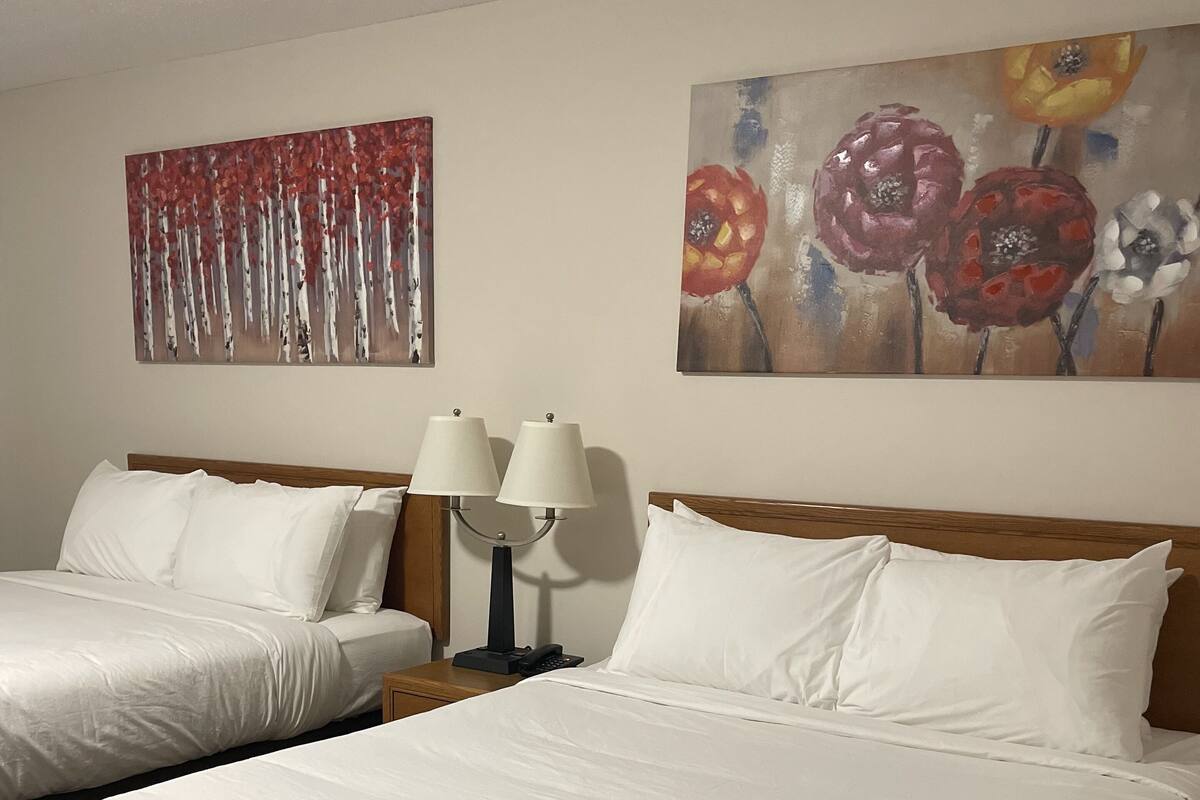 A hotel room with two single beds, a nightstand with lamps, and two paintings on the wall.