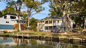 A lakeside property with a modern house, a dock, and a large tree. - Sound Sanctuary: Canal Front w/ Dock, Dog-Friendly (Southern Shores)