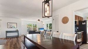 A spacious dining area with a long wooden table, a ceiling fan, and a modern light fixture. - Sound Sanctuary: Canal Front w/ Dock, Dog-Friendly (Southern Shores)