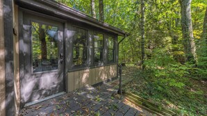 Une cabane dotée d’un porche, entourée d’une forêt.