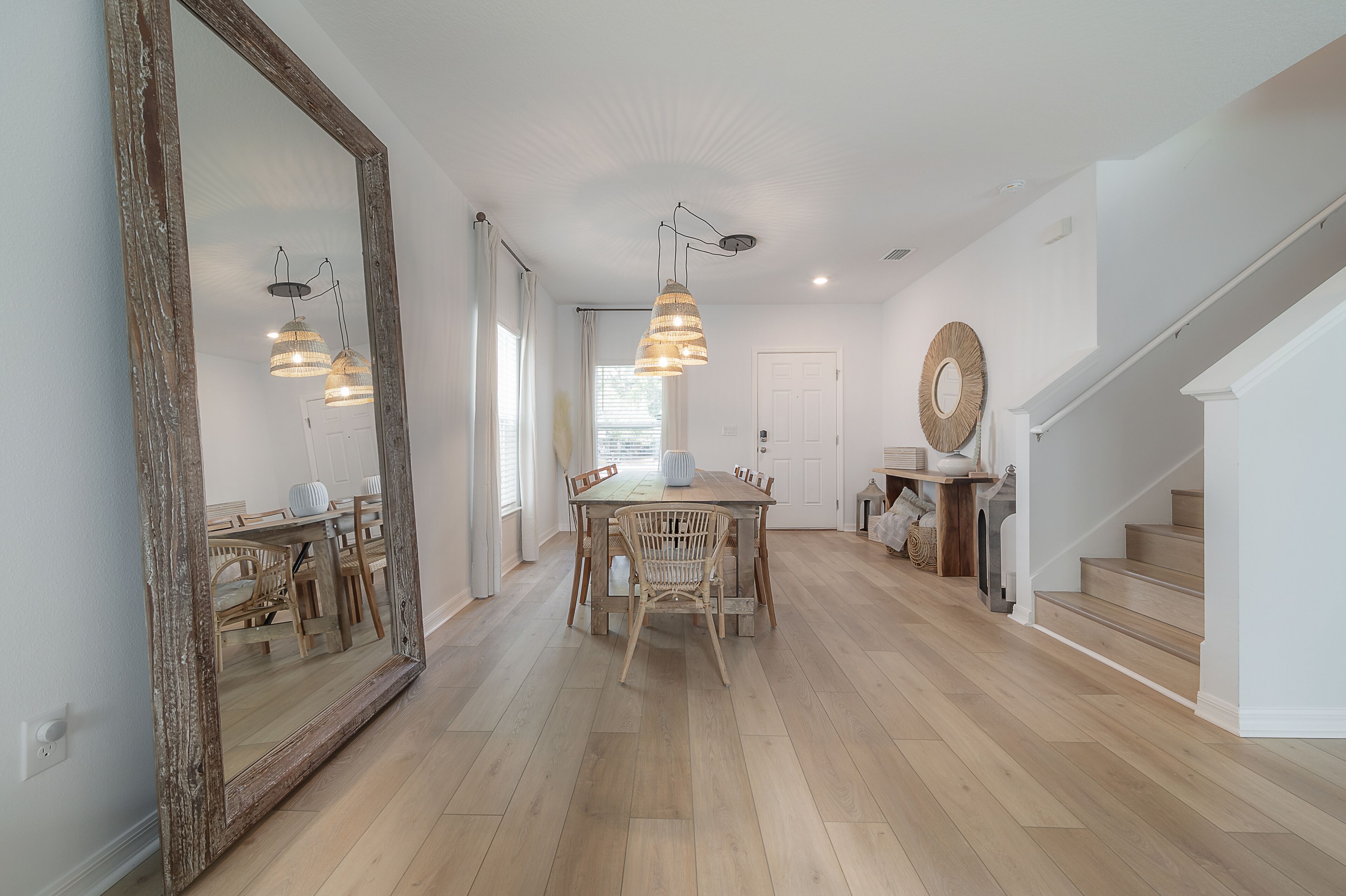 A spacious dining area with a large wooden table and chairs, a hanging pendant light, and a large mirror on the wall.