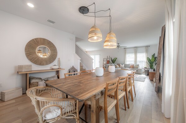 Un vaste espace dédié à la salle à manger, avec une table en bois, des chaises en osier et des luminaires suspendus.