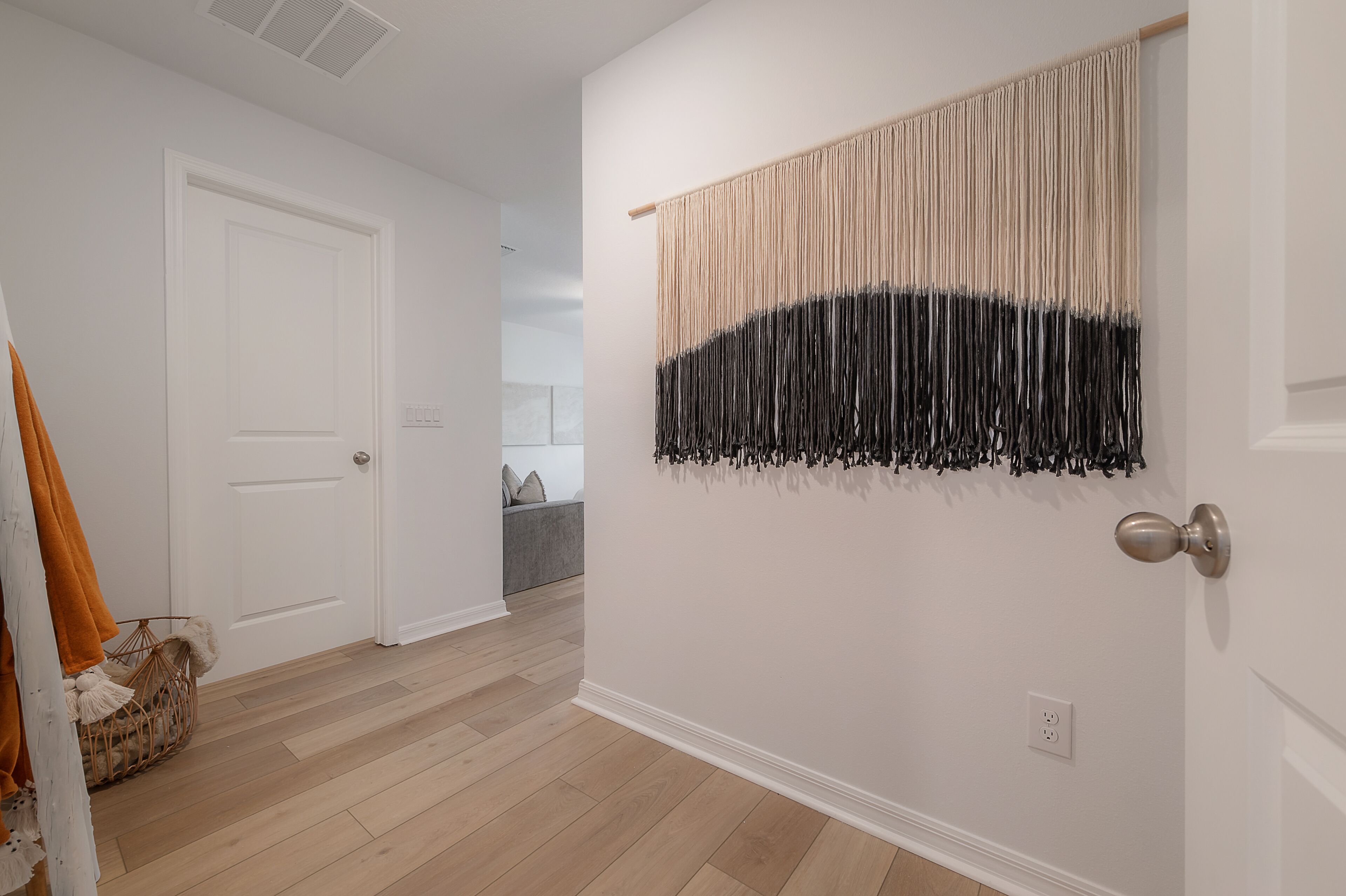 Un couloir avec une porte blanche, un plancher en bois et une tapisserie accrochée au mur.