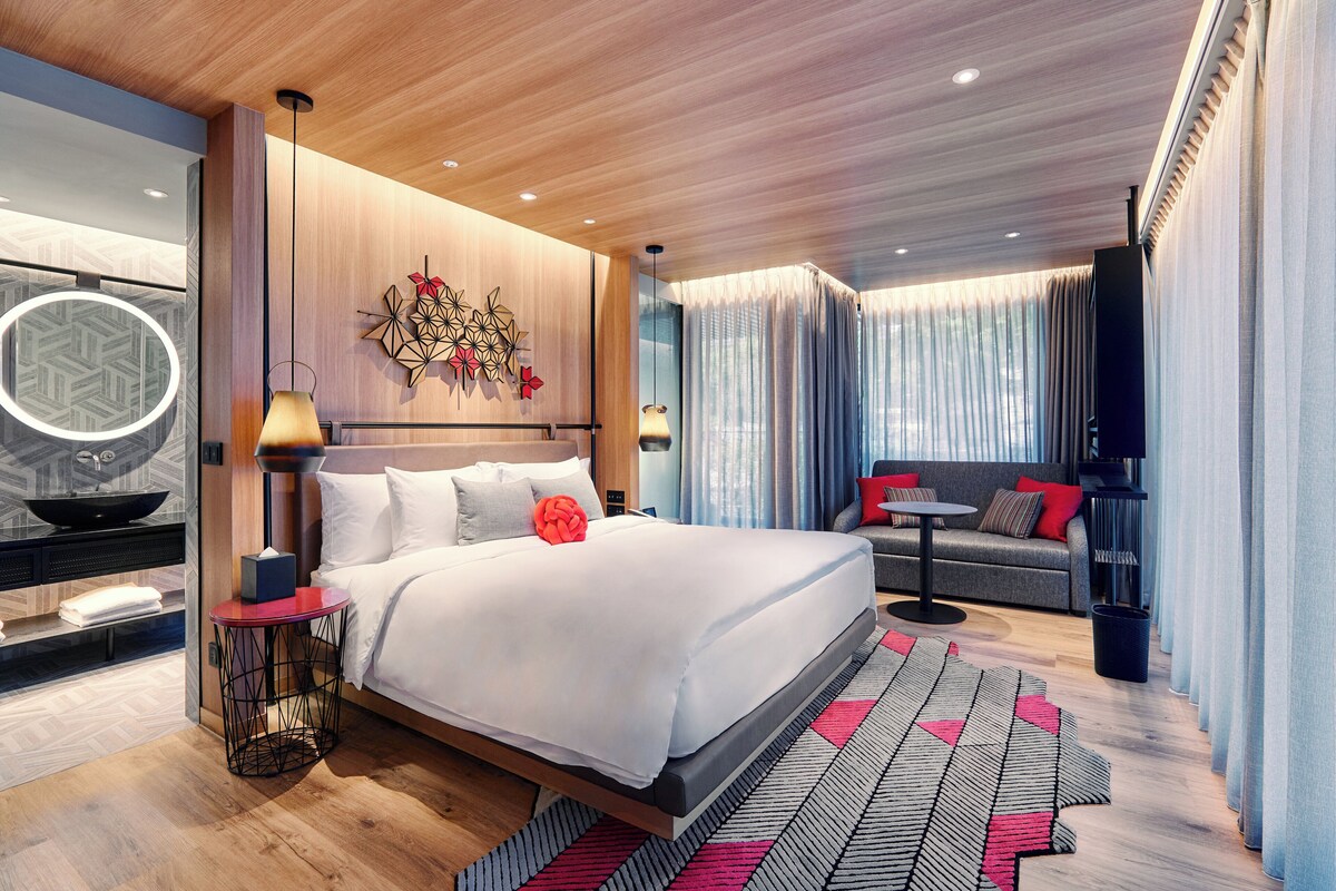A modern hotel room with a large bed, a sofa, a small table, and a decorative wall piece.
