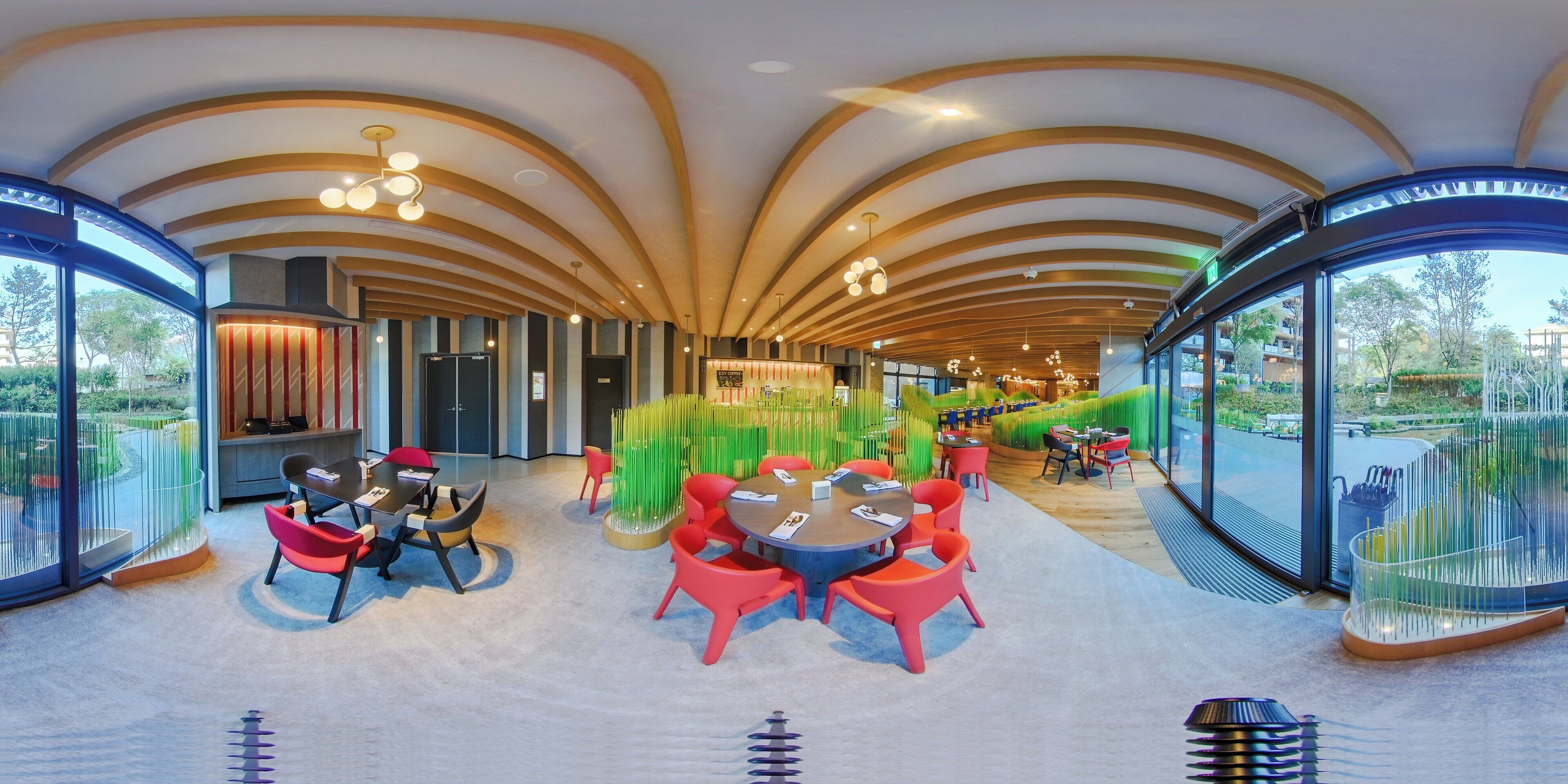 A modern interior with curved wooden beams, a central seating area with round tables and red chairs, and large windows offering a view of greenery.