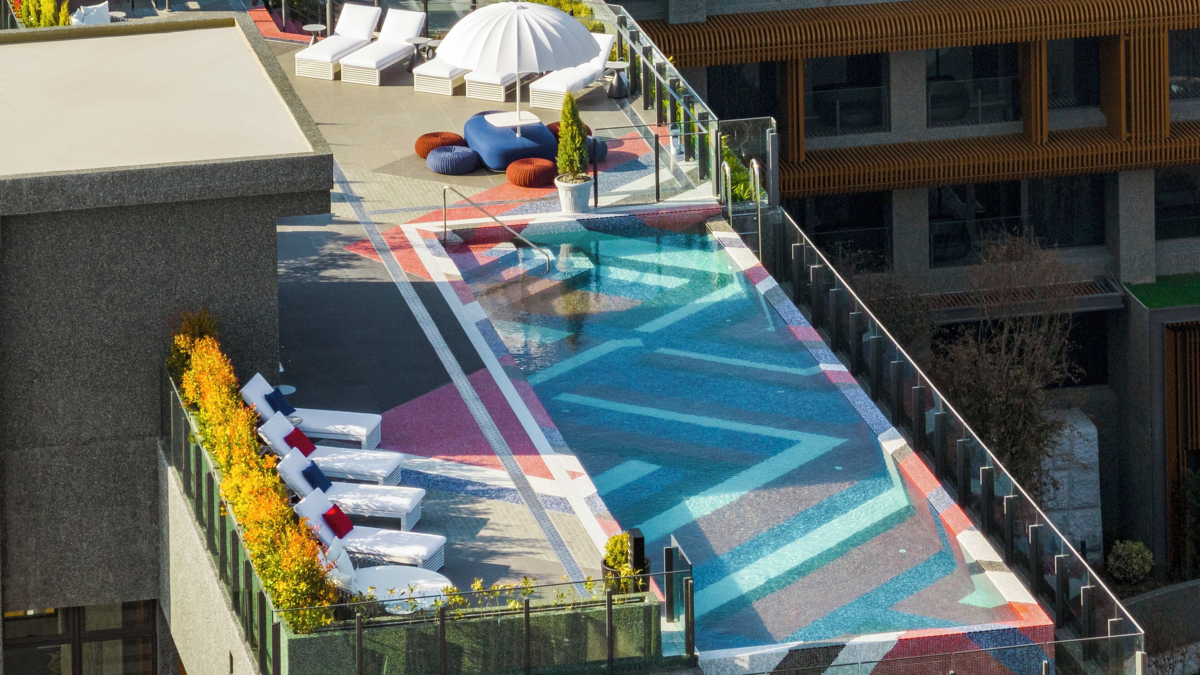 A rooftop pool with lounge chairs and a colorful geometric-patterned floor.