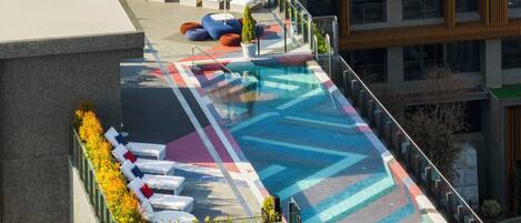 A rooftop pool with lounge chairs and a colorful geometric-patterned floor.