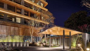 Een modern hotel met een overdekte ingang, een terras buiten en een goed verlichte gevel 's nachts.