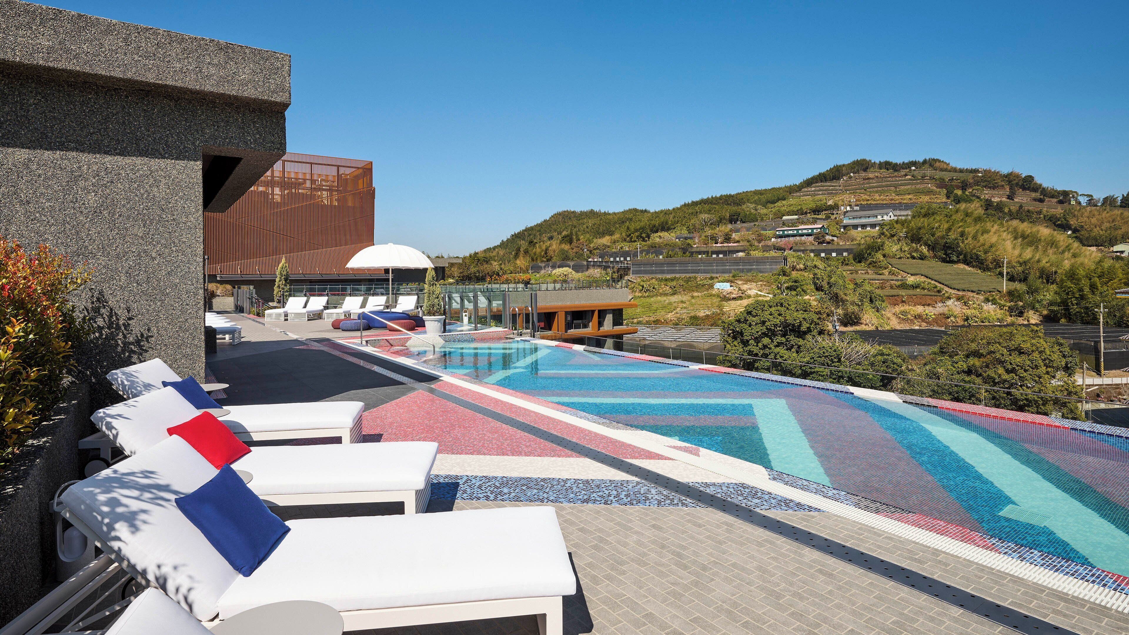 A rooftop pool area with lounge chairs and a view of a hilly landscape.