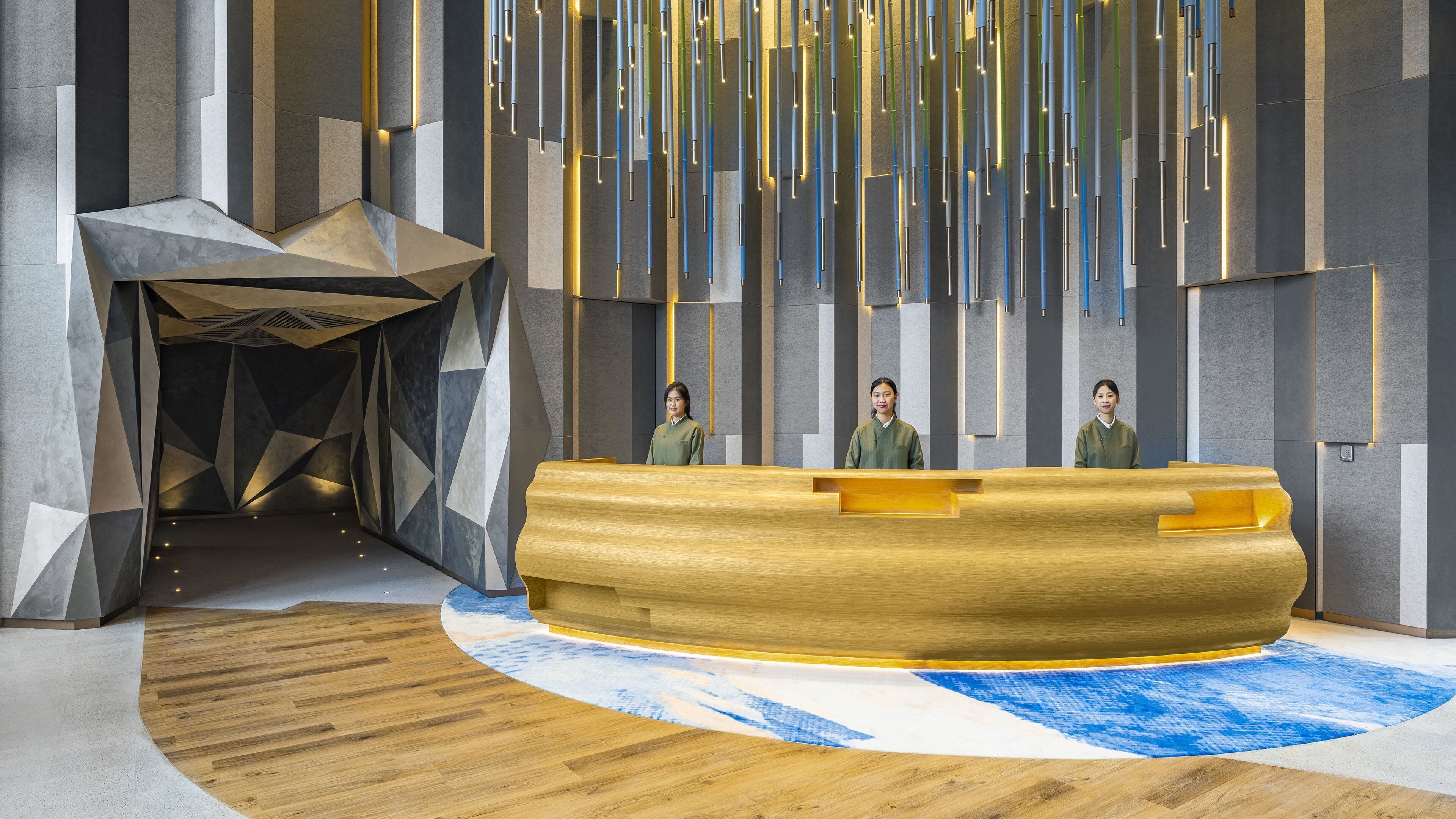 Un área de recepción moderna con un mostrador de madera, patrones geométricos en la pared y lámparas colgantes.