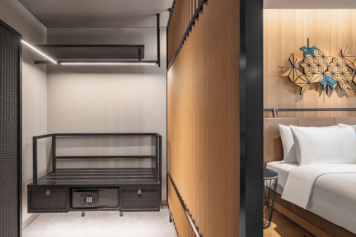 A modern bedroom with a minimalist design, featuring a bed, a small desk, and a decorative wall piece.