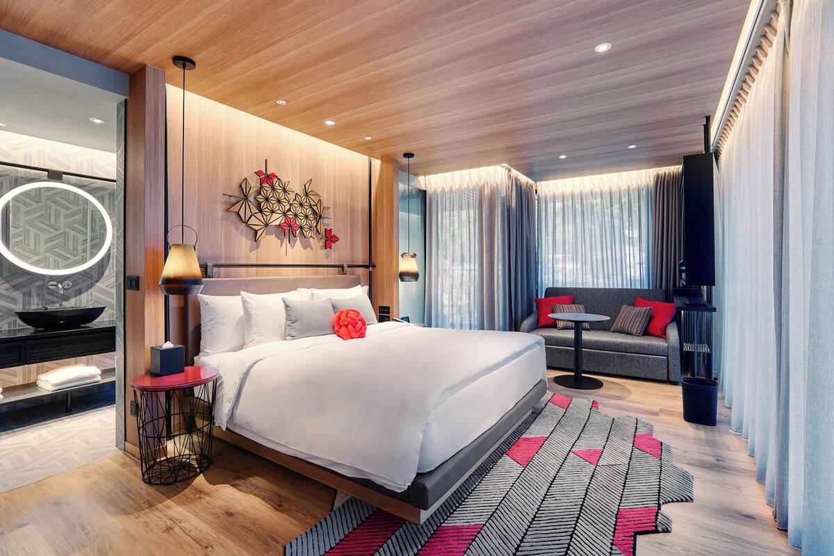 Ein modernes Hotelzimmer mit einem großen Bett, einer Couch, einem kleinen Tisch und einer Wanddekoration.