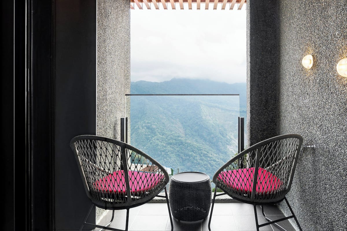 Ein Balkon mit zwei Korbstühlen und einem kleinen Tisch, mit Blick auf eine Berglandschaft.