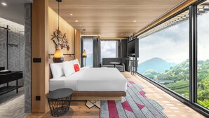 Een moderne slaapkamer met een groot bed, een klein tafeltje en een televisie. Er is een houten plafond en grote ramen met uitzicht op het landschap.