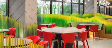 Un restaurante moderno con mesas redondas y sillas rojas, que destaca por un llamativo diseño de pared verde y amarillo.