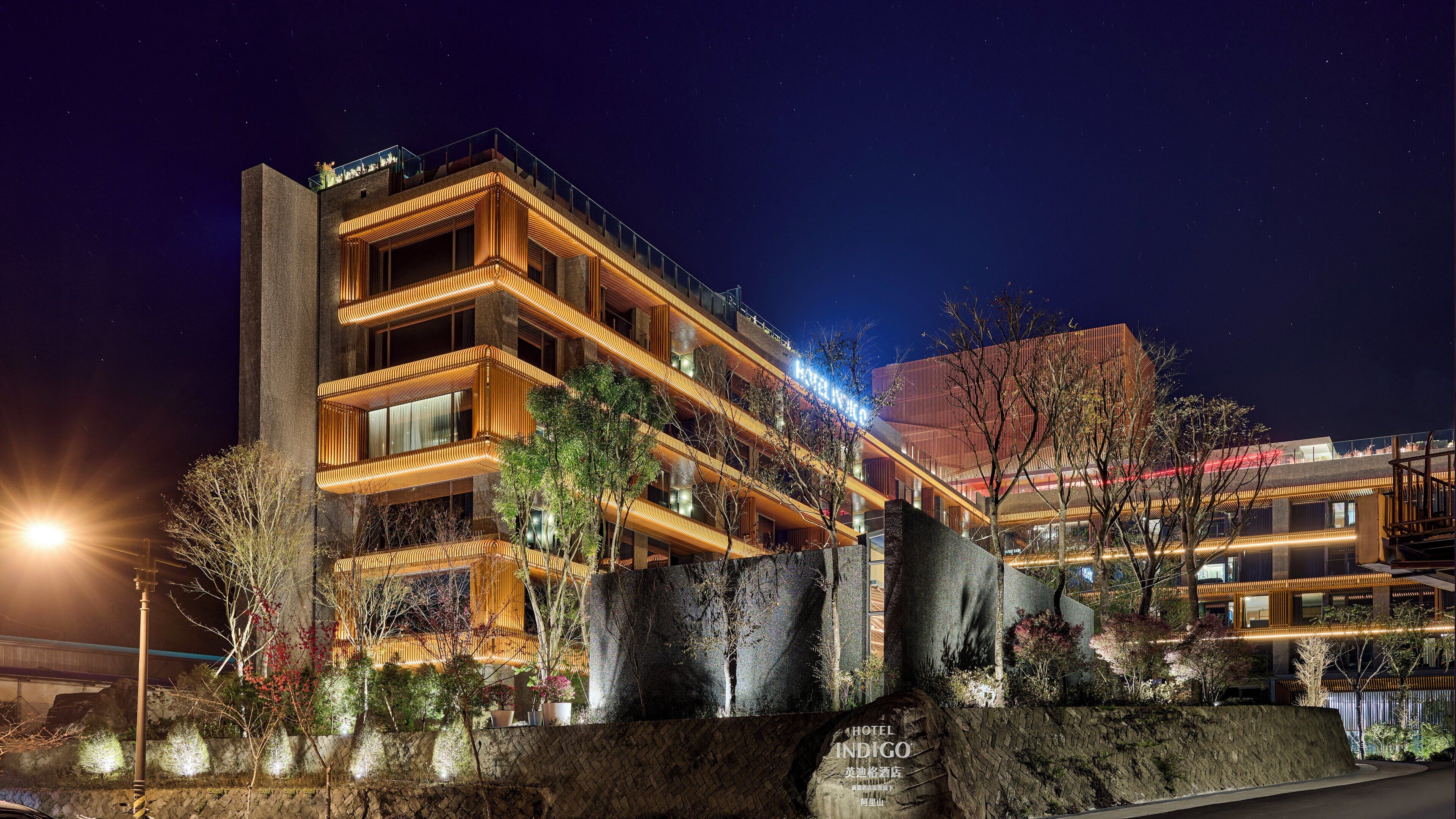 Un hotel moderno con varios balcones, fachada de piedra y una entrada bien iluminada.