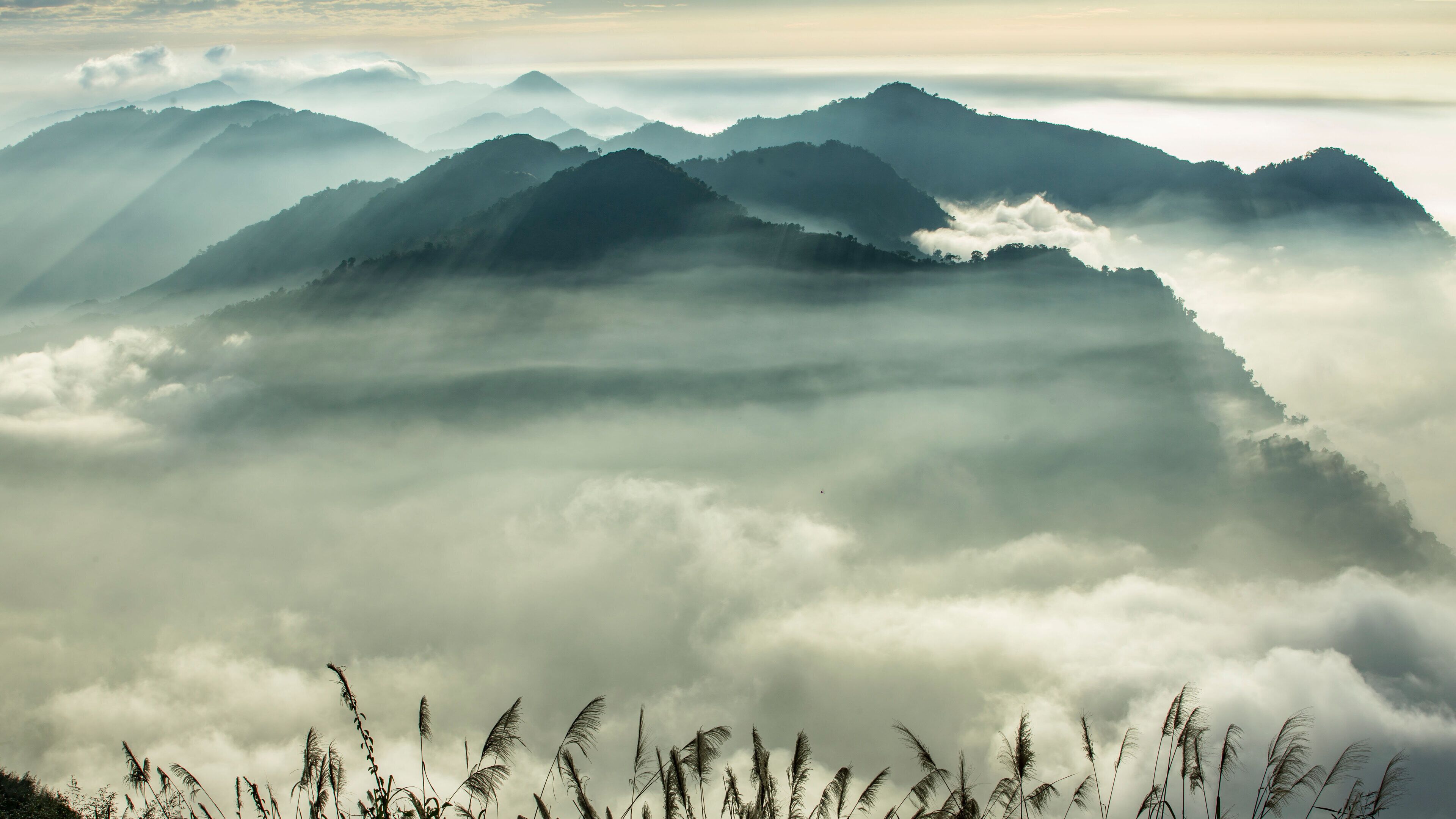 A mountainous landscape with a valley of clouds and grass at the base.