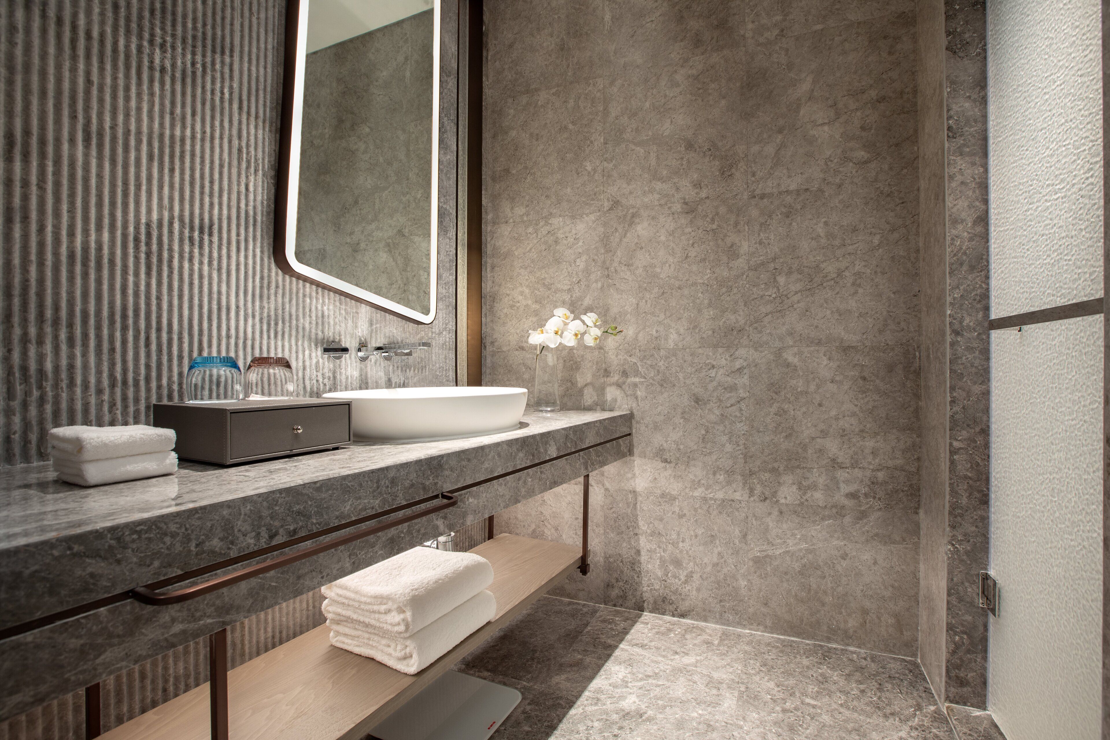 A modern bathroom with a large mirror, a vessel sink, and a shower area.