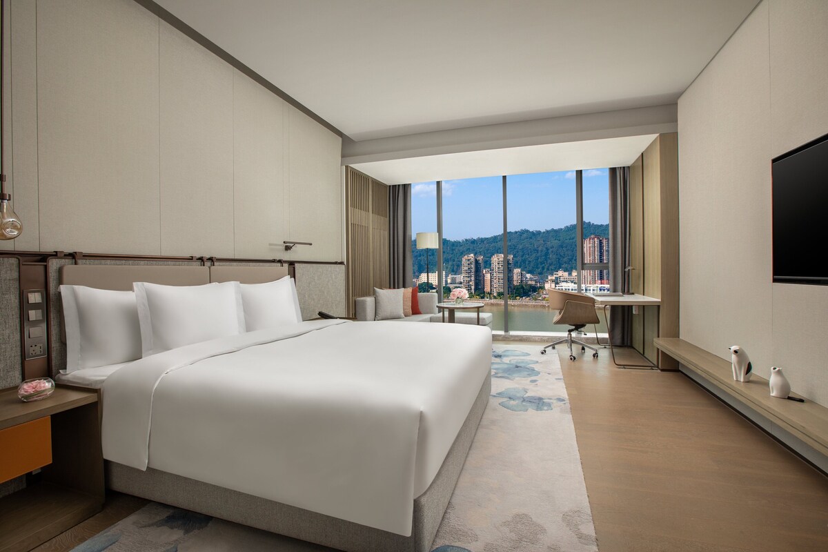 A hotel room with a large bed, a desk, and a view of a cityscape.