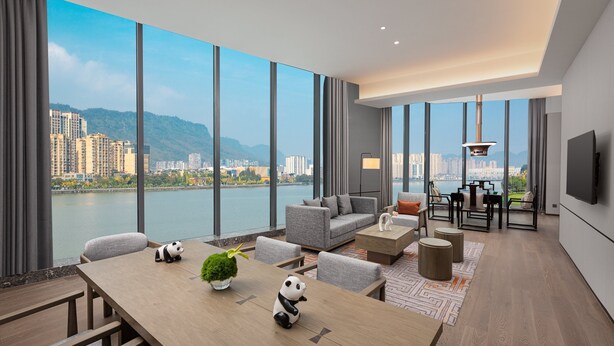 Una sala de estar moderna con un ventanal grande, un sofá, una mesa de comedor con sillas y un televisor montado en la pared.