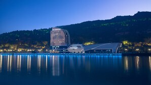 Un hotel moderno con fachada de vidrio curva y techo plano, ubicado junto a una masa de agua con reflejos.