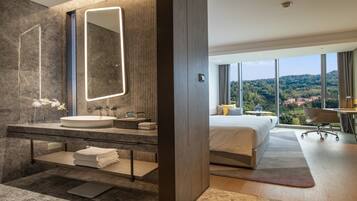 A modern hotel room with a large bed, a bathroom with a vanity, and a view of the landscape.