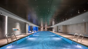 Una piscina interior moderna con agua cristalina, sillas de descanso y un largo banco.