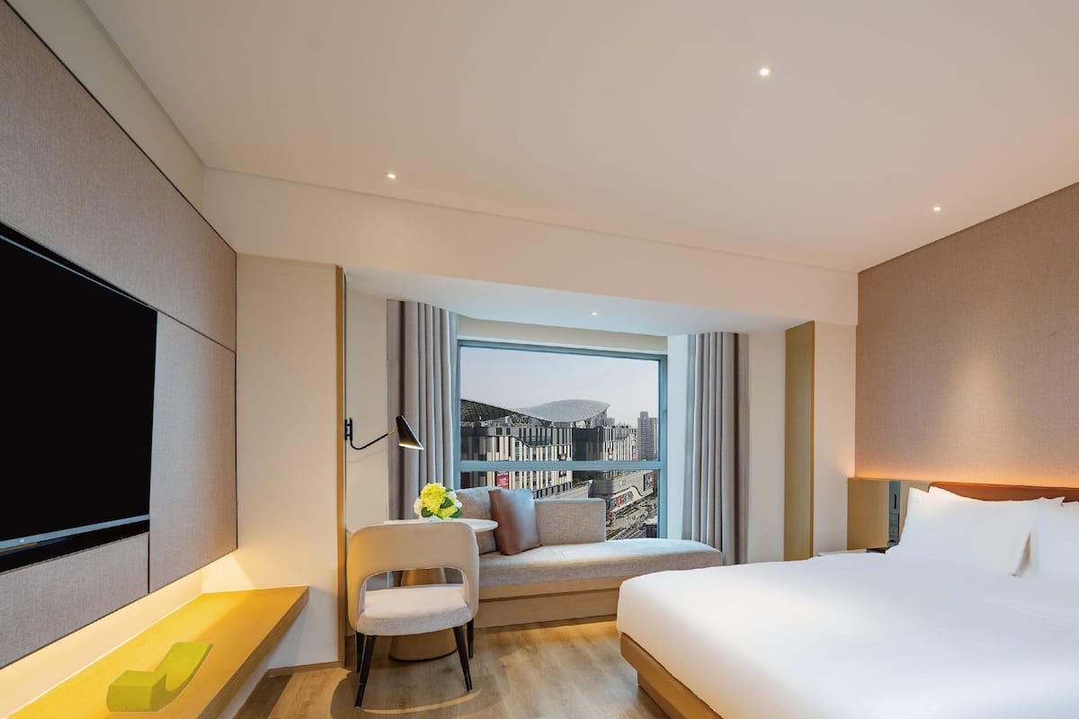 A modern hotel room with a large bed, a desk, a chair, and a TV.