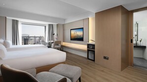 Habitación de hotel moderna con una cama grande, un escritorio con ordenador, televisor y vistas a la ciudad.