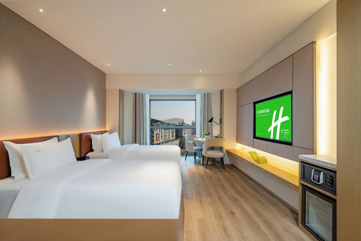 A modern hotel room with a large bed, a desk, a television, and a view of the city.