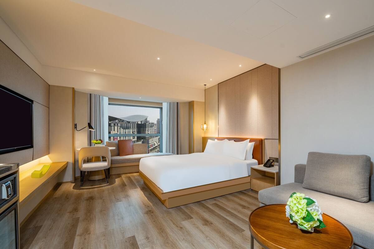 A modern hotel room with a large bed, a sofa, a small table, and a TV.
