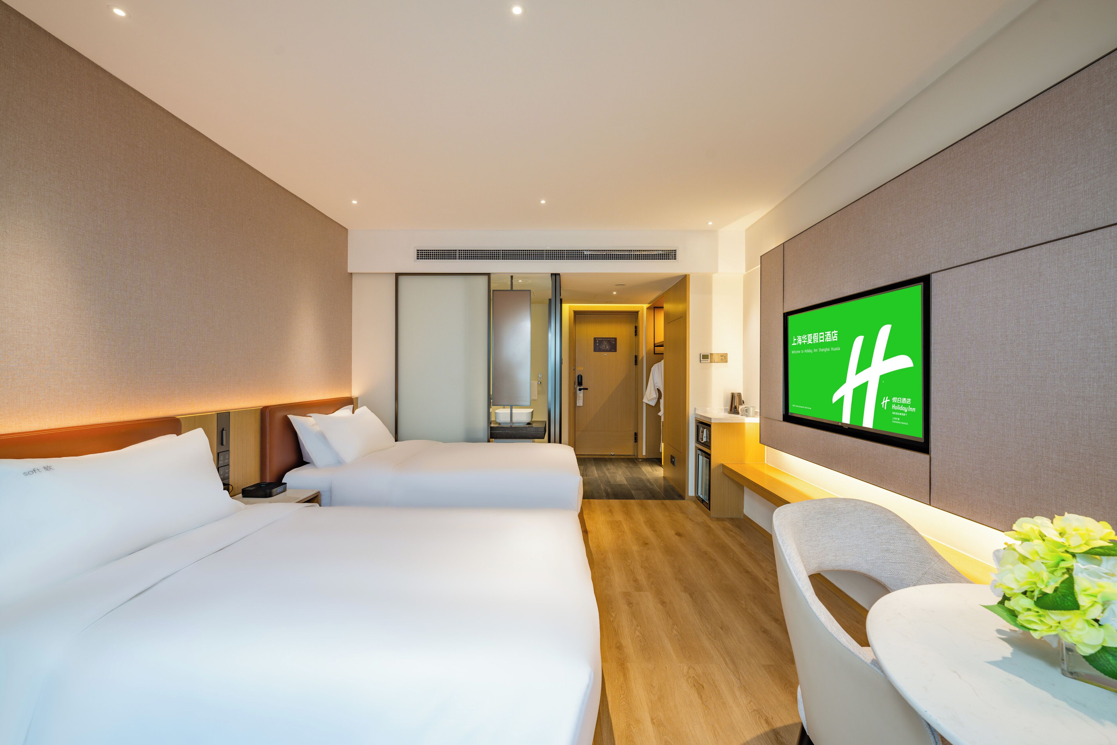 Habitación de hotel con dos camas, un escritorio, una silla y un televisor montado en la pared.
