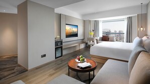 Habitación de hotel moderna con una cama grande, un escritorio, un televisor y vistas a la ciudad.