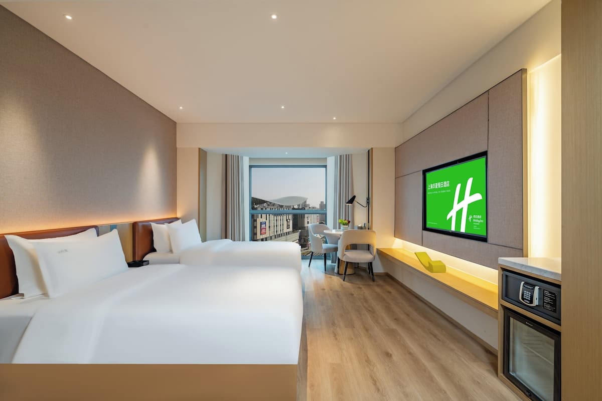 A modern hotel room with a large bed, a desk, a television, and a view of the cityscape.