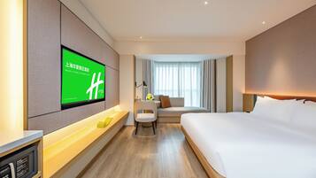 A hotel room with a large bed, a desk with a computer, a TV mounted on the wall, and a sofa.