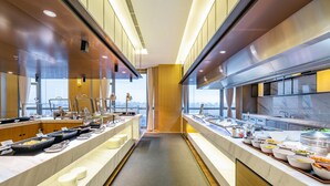 Cocina de hotel moderna con una larga barra de buffet, encimeras de mármol y vistas de la ciudad a través de amplias ventanas.
